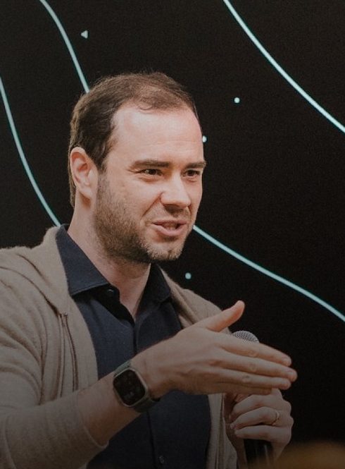 Andrej Karpathy speaking on stage, microphone in hand.